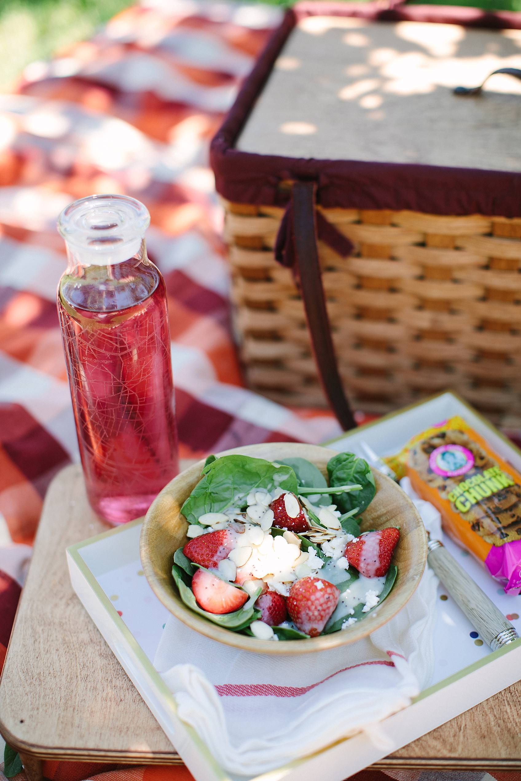 picnic basket in background on blanket featuring strawberry spinach salad with goat cheese