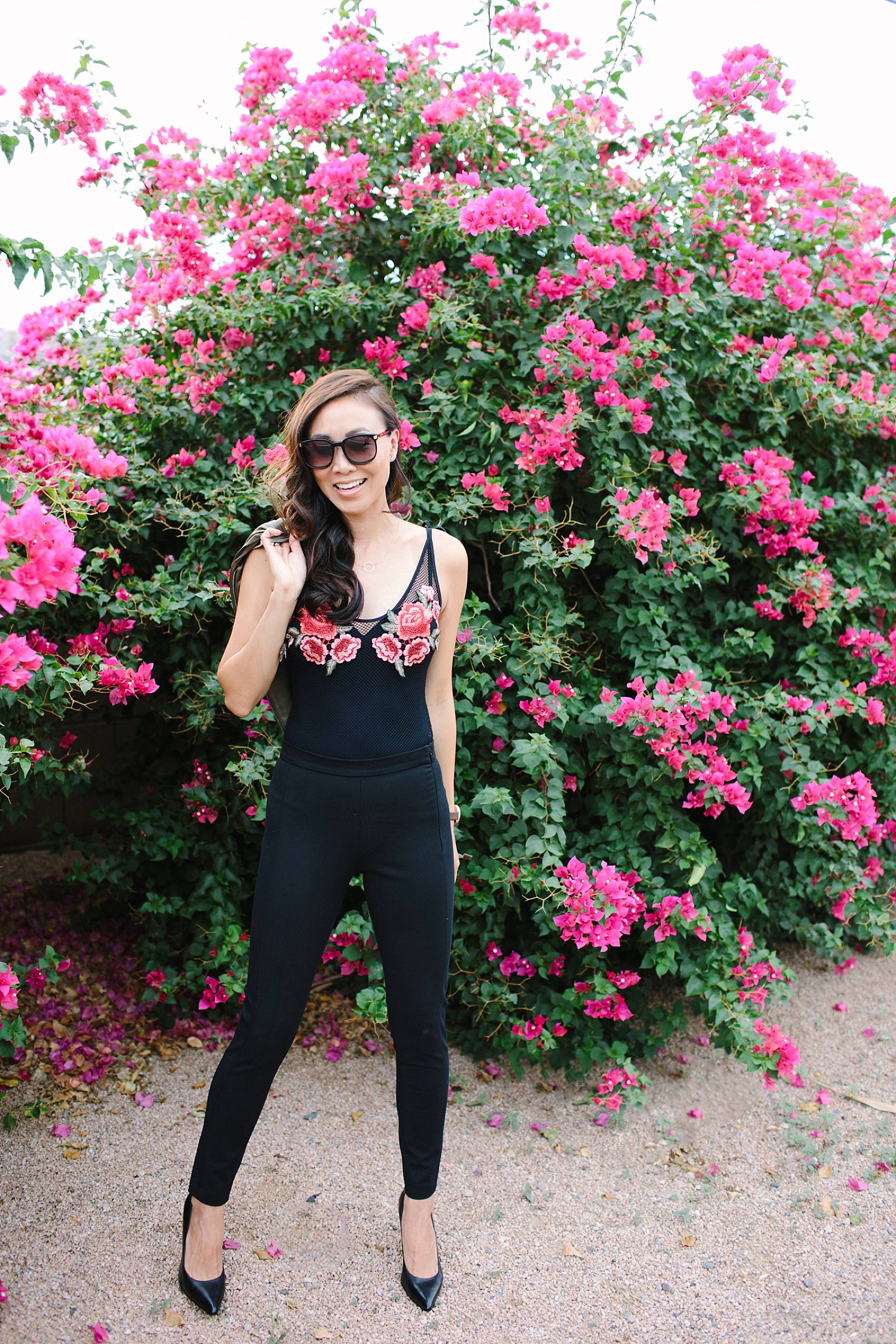 diana elizabeth lifestyle blogger in black devon-fit bi-stretch leggings and satin bomber jacket by banana republic standing in front of pink bougevvilla plants 