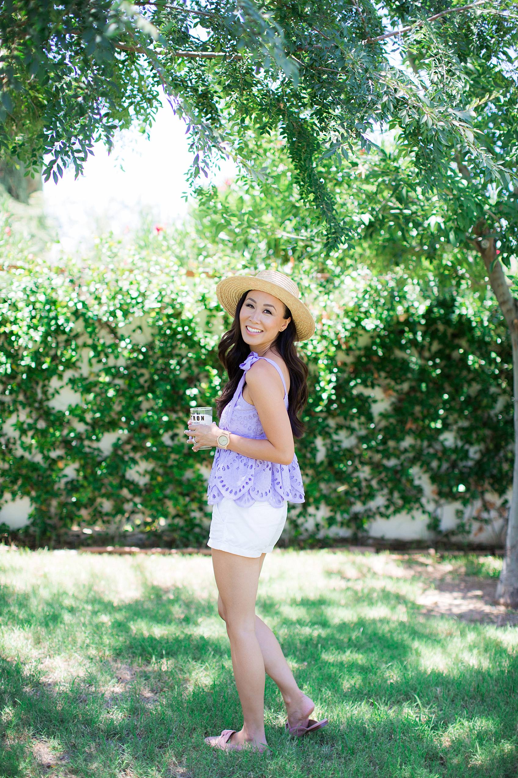 Lifestyle blogger diana elizabeth in purple eyelet top by j.crew in backyard jasmine vine wall holding glass of lemonade
