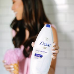holding dove beauty wash in shower with ice cream body pouf