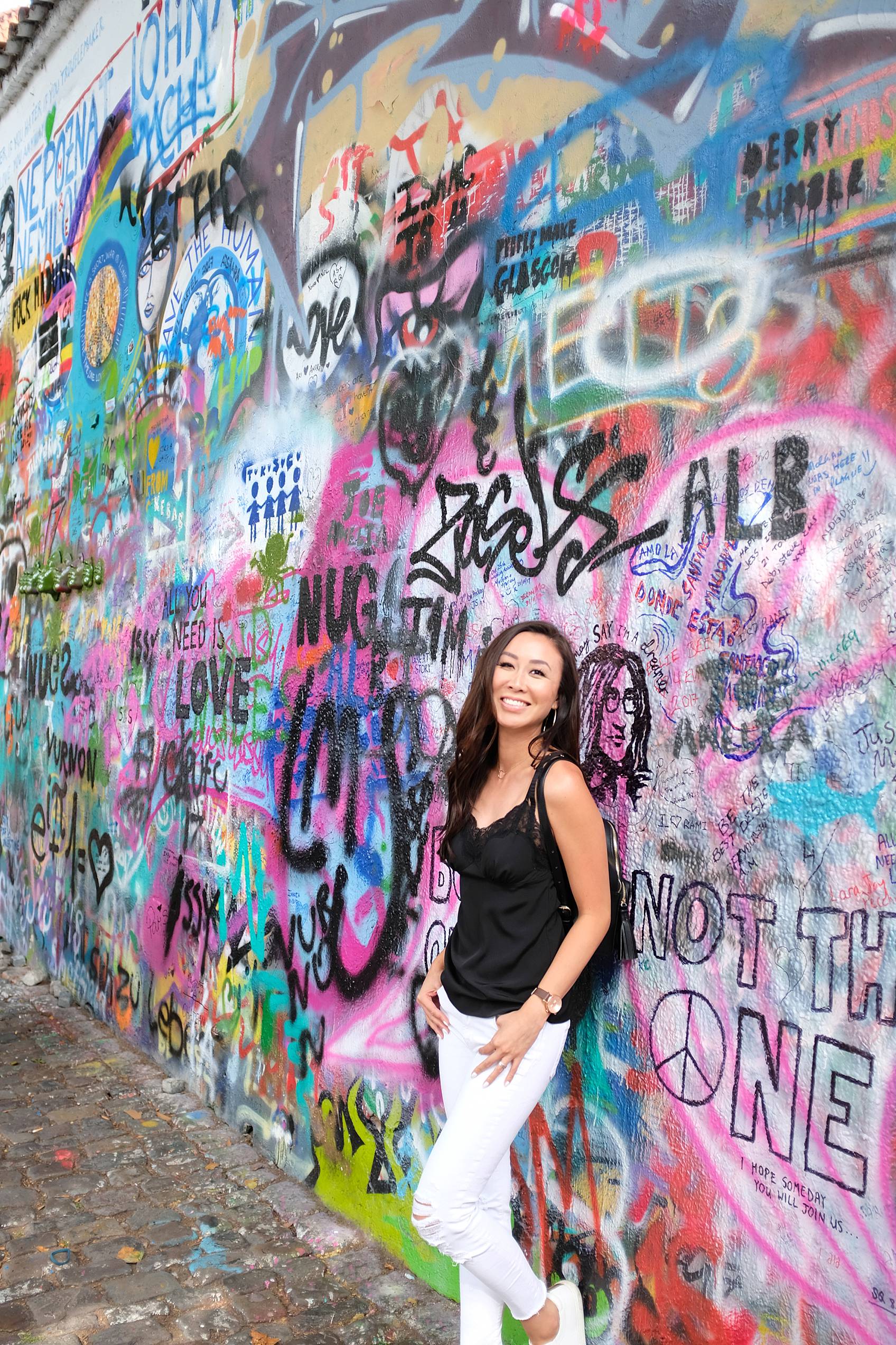 Diana Elizabeth lifestyle blogger leaning against graffiti wall called John Lennon wall in Prague