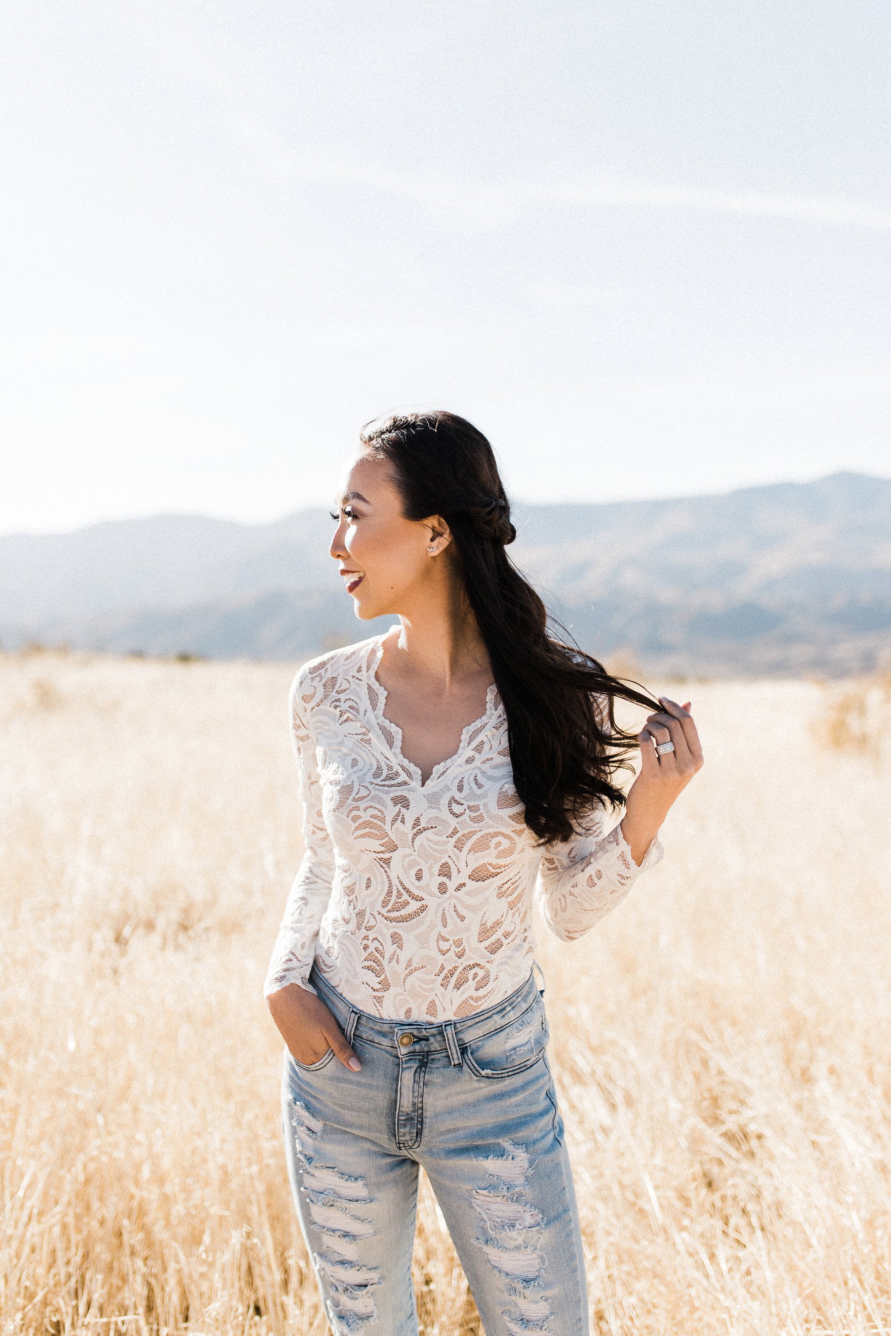 wind in hair white lace bodysuit high waist ripped jeans in a field Diana Elizabeth blogger photography by Autumn Renae