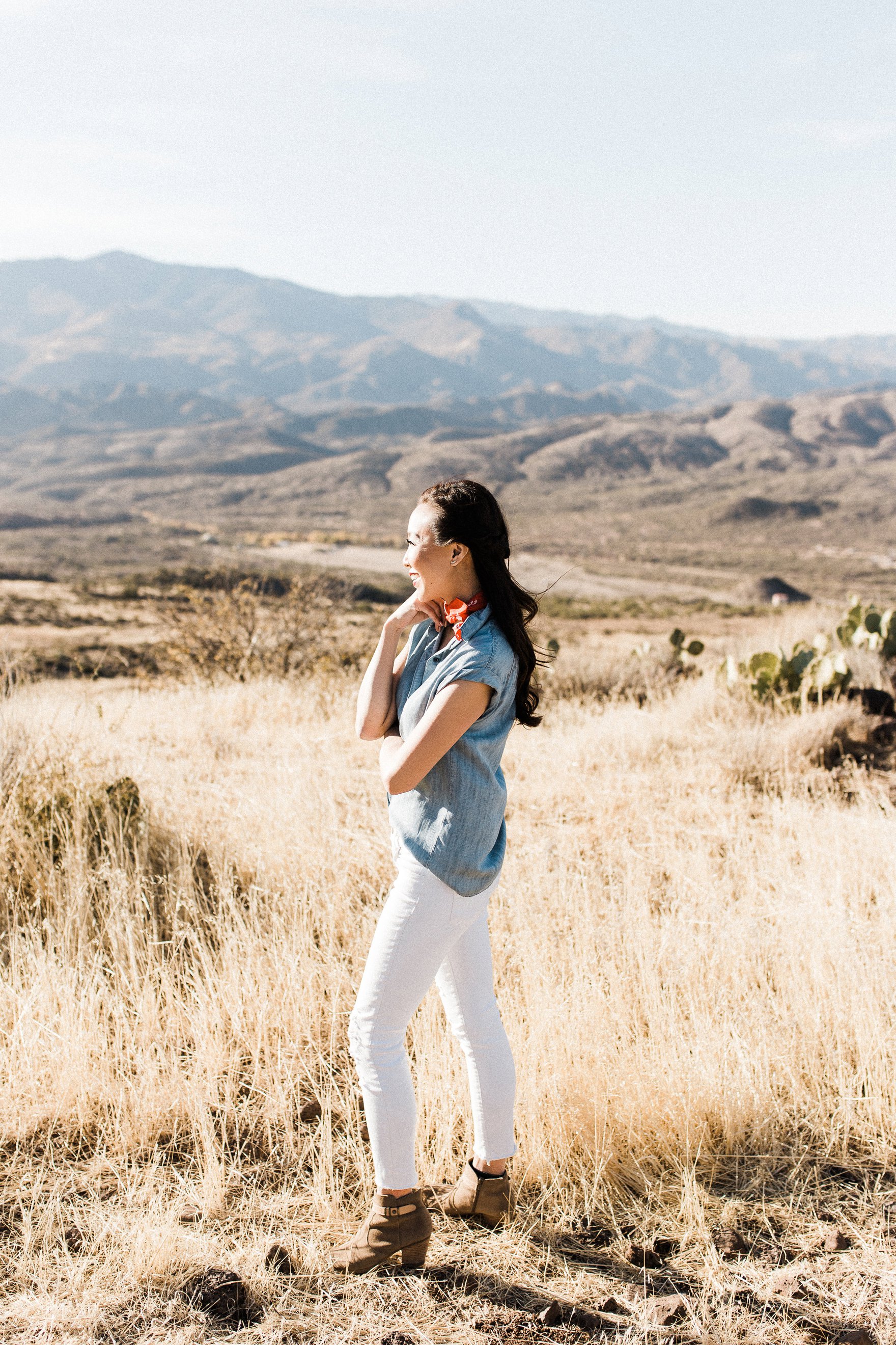 chambray short sleeved shirt white jeans with booties in tall dry grass in the arizona phoenix desert wearing red scarf around neck