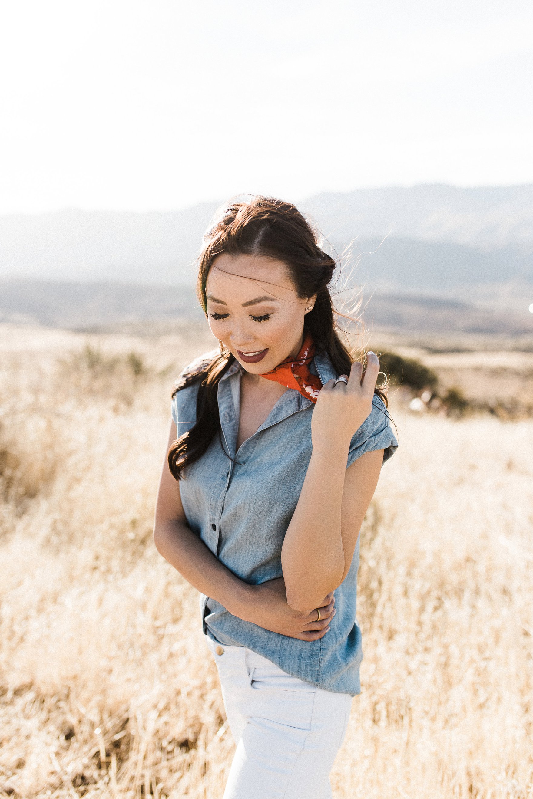 chambray short sleeved shirt white jeans with booties in tall dry grass in the arizona phoenix desert wearing red scarf around neck