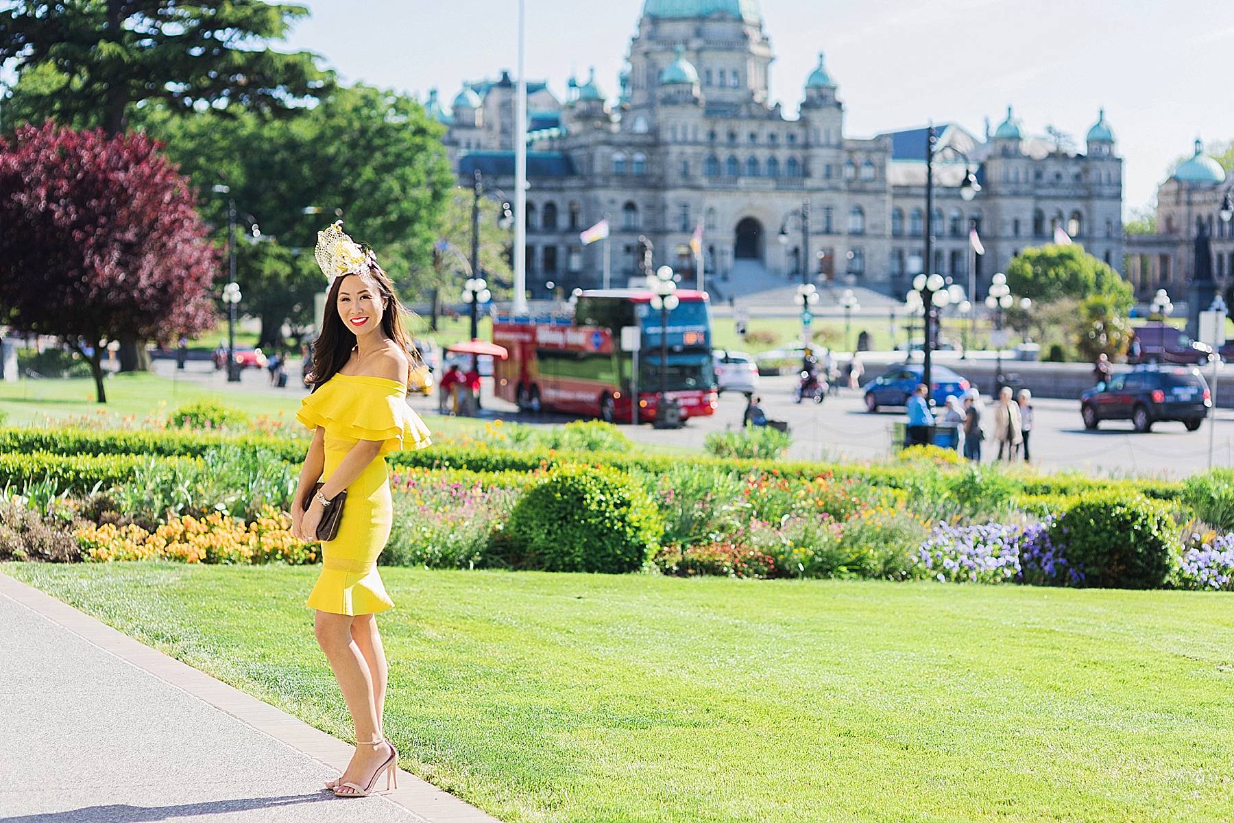 yellow fascinator hat bee hive high tea for bridal shower wedding celebration at empress hotel Victoria Canada wearing yellow off shoulder ruffle dress on blogger Diana Elizabeth standing in front of the Parliament building