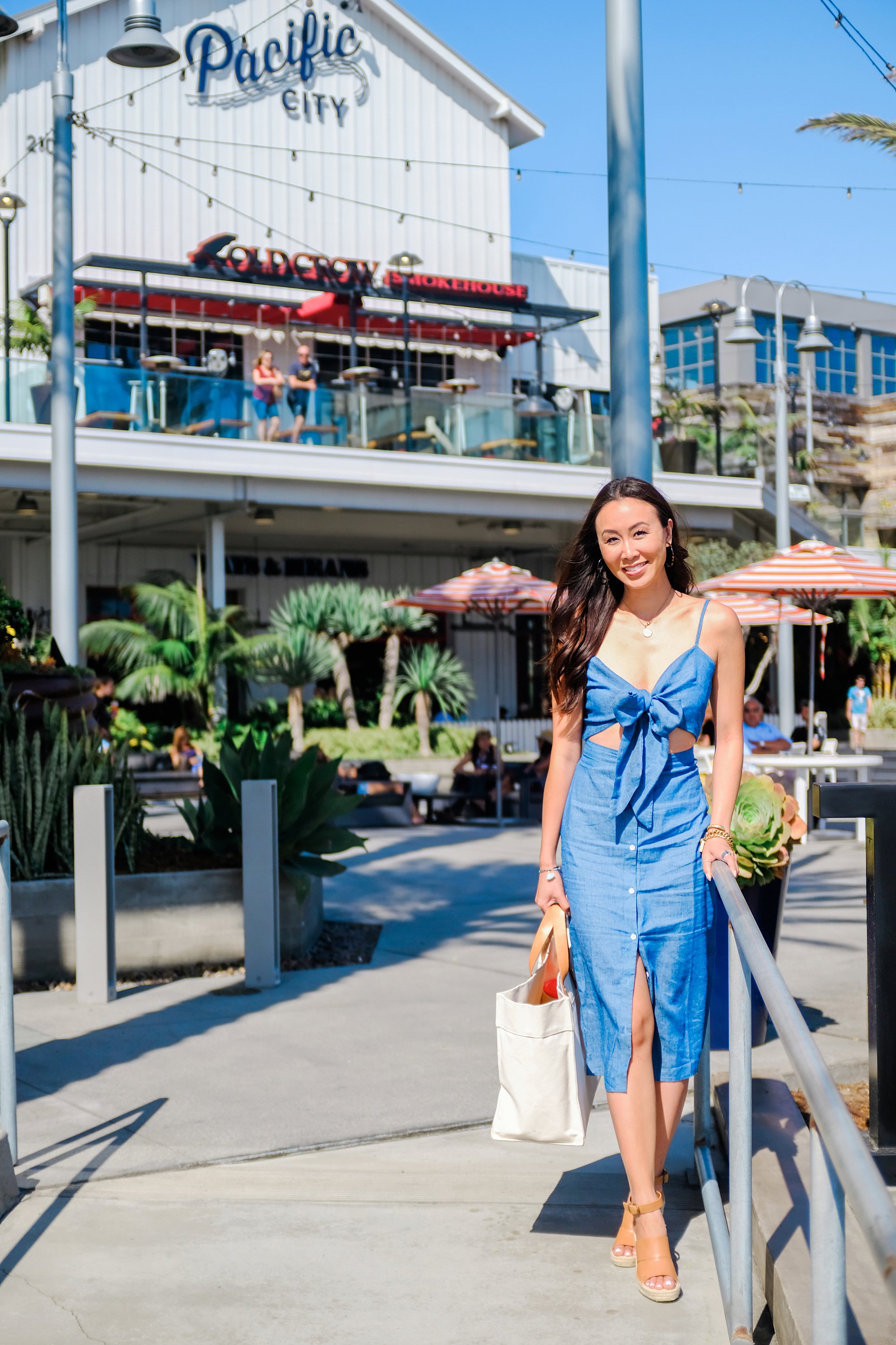 blue tie front button down midi dress misguided, lifestyle Phoenix blogger Diana Elizabeth walking at pacific City Huntington Beach carrying beach tote