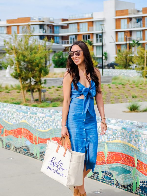 blue tie front button down midi dress misguided, lifestyle Phoenix blogger Diana Elizabeth walking at pacific City Huntington Beach carrying beach tote sitting on tile bench