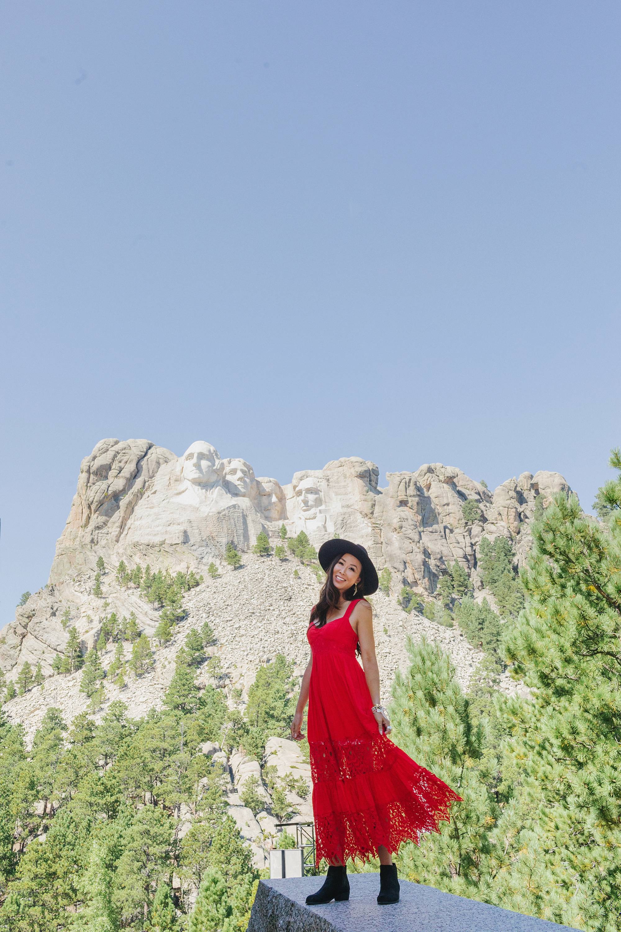 Mount Rushmore in south Dakota posing is Diana Elizabeth lifestyle blogger wearing free people red maxi dress and black wool hat