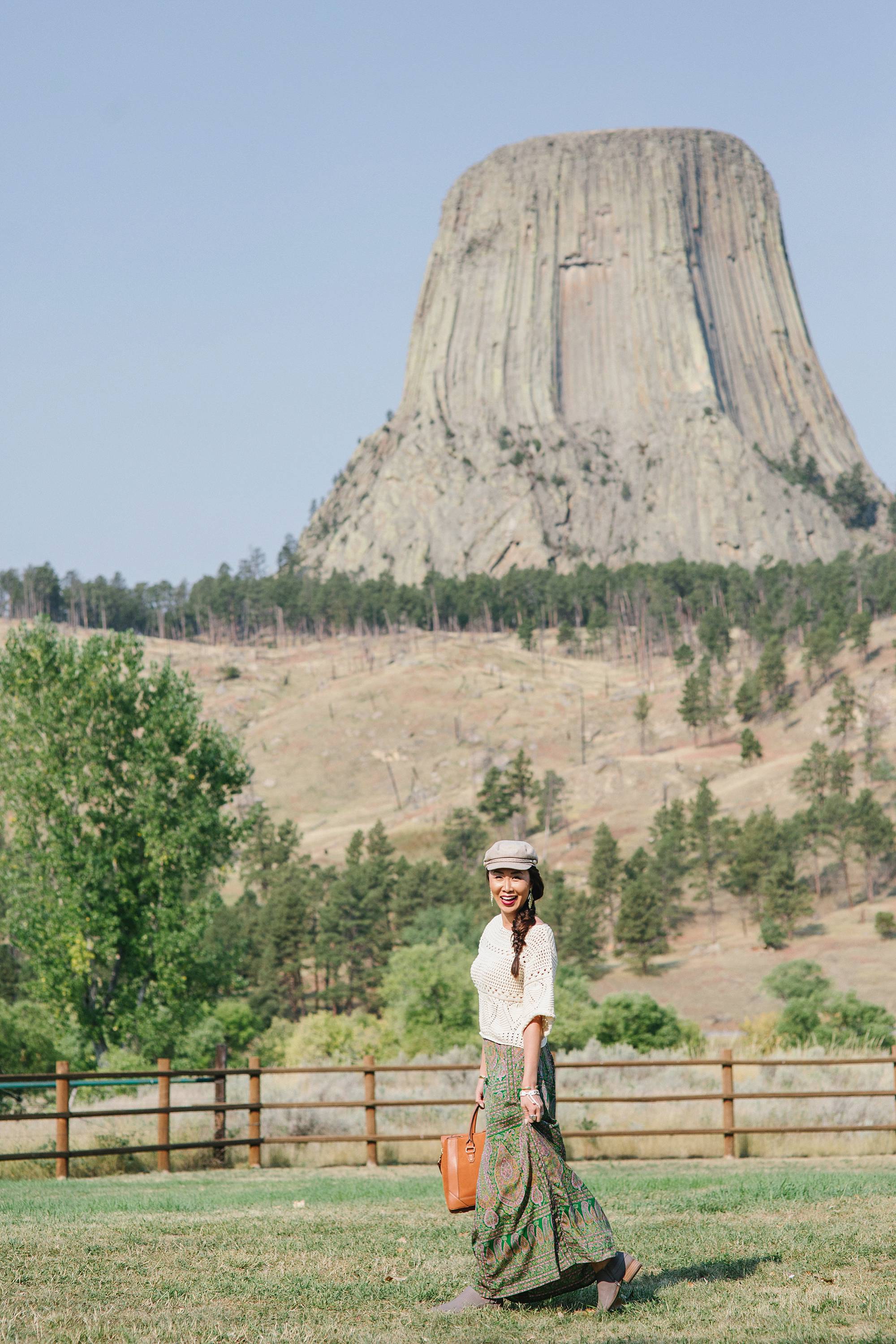 devil's tower in Wyoming, lifestyle blogger Diana Elizabeth in paisley skirt and open kit sweater and India hicks leather handbag