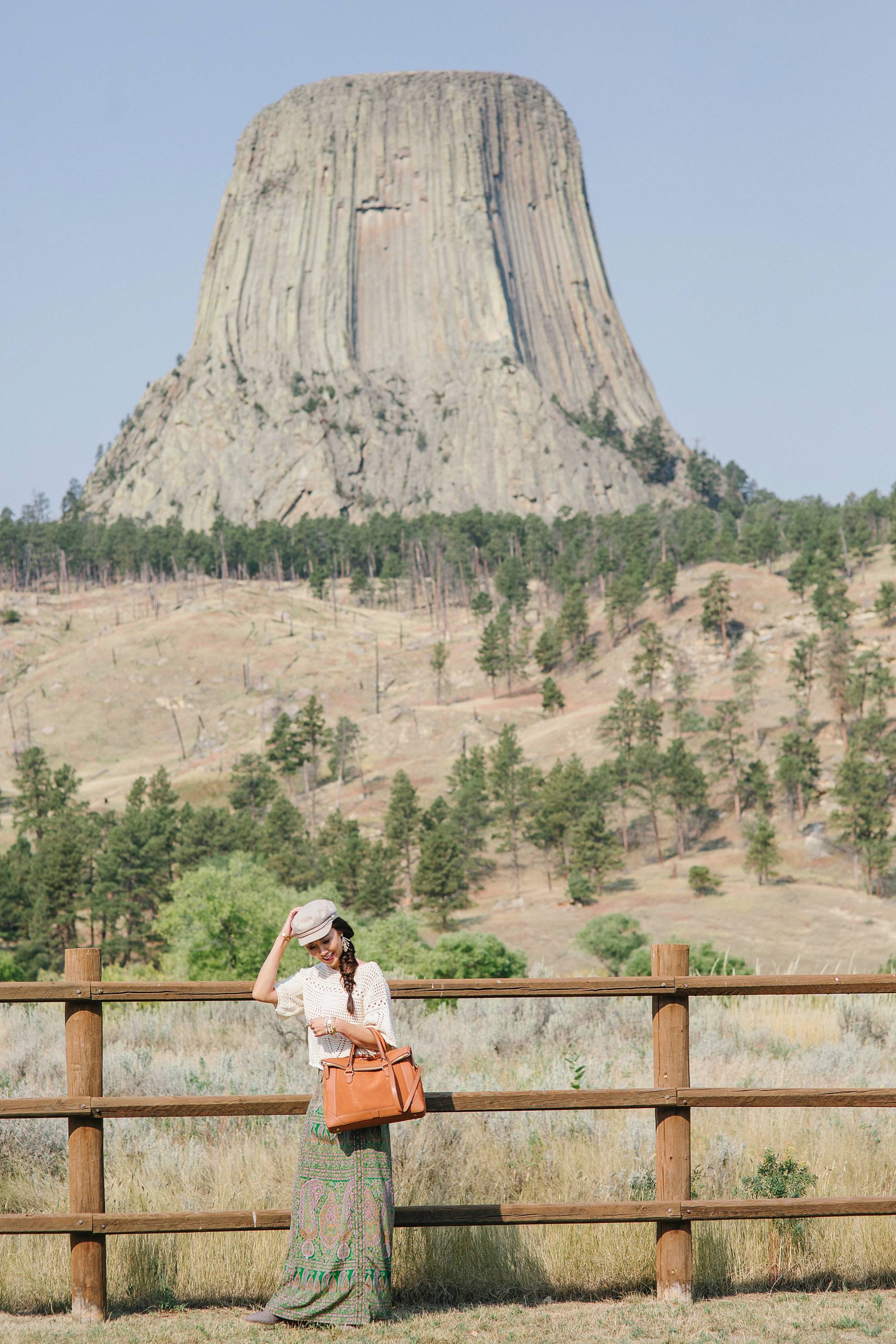 devil's tower in Wyoming, lifestyle blogger Diana Elizabeth in paisley skirt and open kit sweater and India hicks leather handbag
