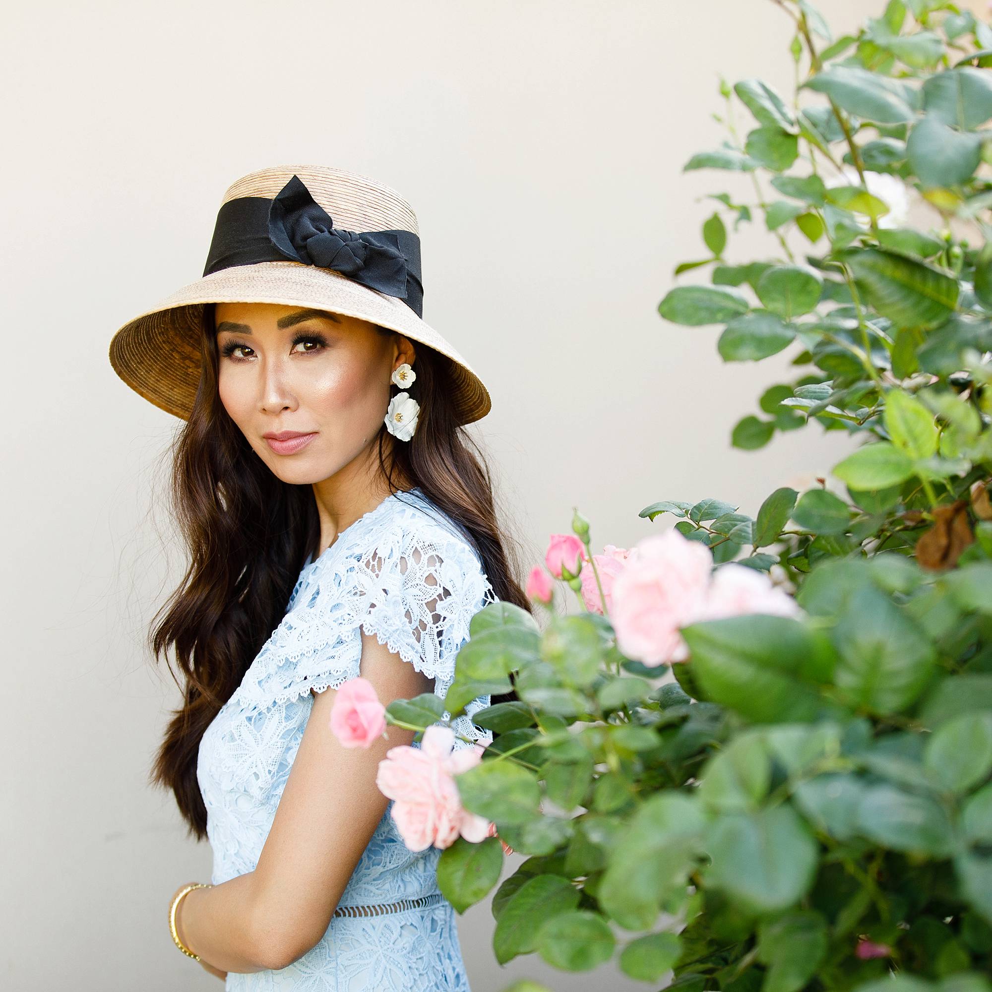 blue lace dress with garden hat from terrain nestled between pink roses against the wall - lifestyle blogger Diana Elizabeth phoenix scottsdale arizona holding rose