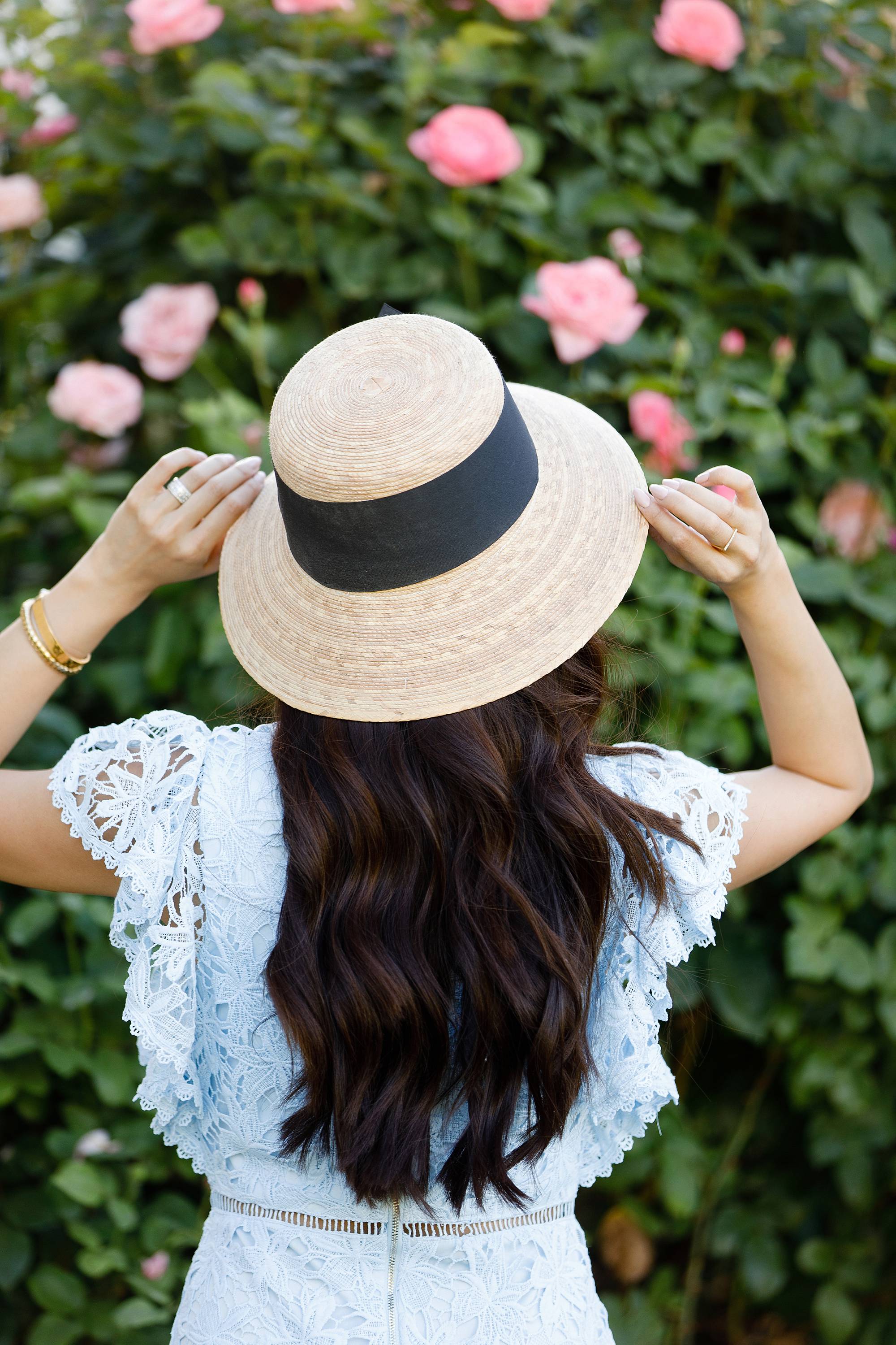 woman hands on hat pose blue lace dress with garden hat from terrain nestled between pink roses against the wall - lifestyle blogger Diana Elizabeth phoenix scottsdale arizona