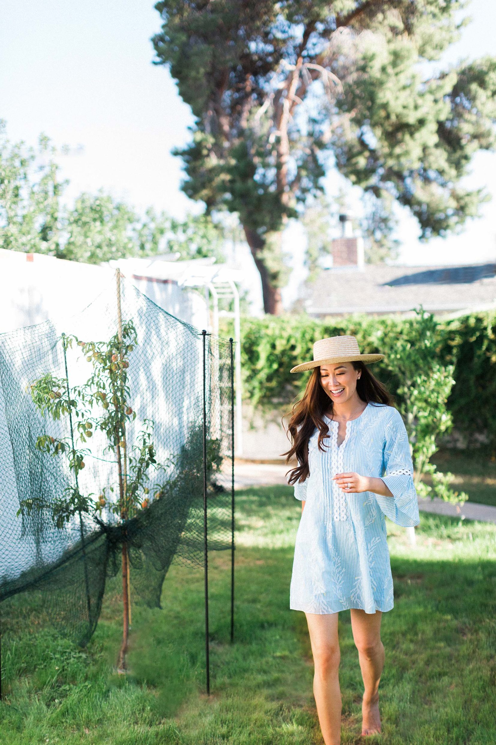 running through home backyard orchard peach tree barefoot in lightweight dress and straw hat
