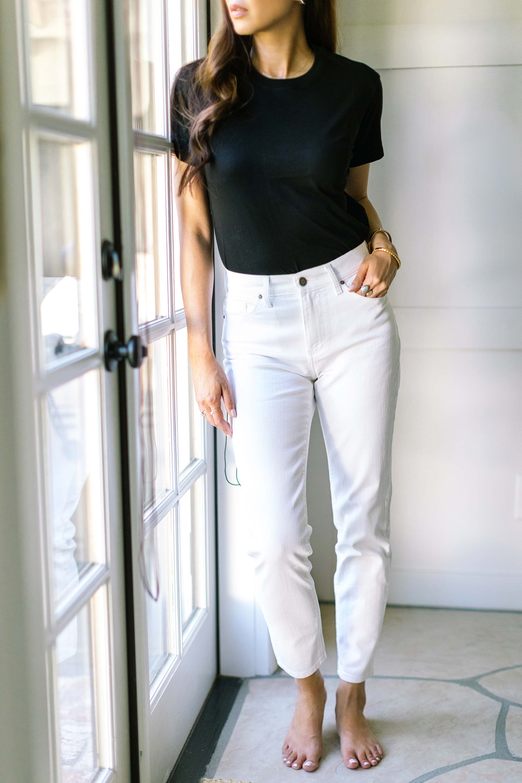 Diana Elizabeth phoenix lifestyle blogger in white pants blacks shirt leaning against black and white bone dresser by lots of house plants. jeans and top by Mott and bow