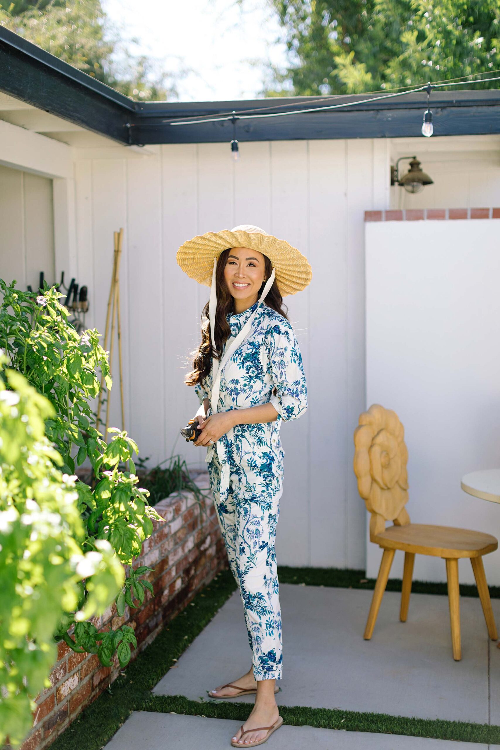 blue and white print jumpsuit wearing straw hat gardening in Phoenix Arizona lifestyle blogger talking about home ownership dreams
