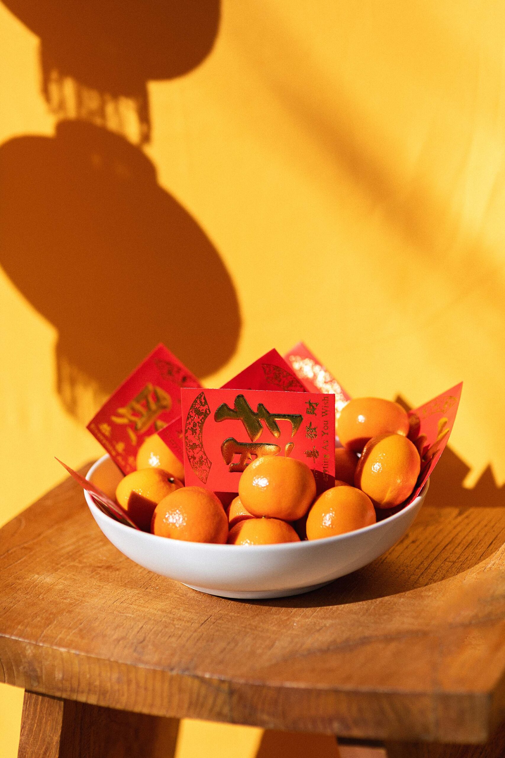 mandarin oranges in a bowl with red envelopes Chinese New Year - Chinese New Year lunar new year outfit and festivities - growing up Asian American blog post - DianaElizabethblog.com